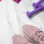 Flat lay of pastel pink fitness gear including sneakers and dumbbells on marble texture.